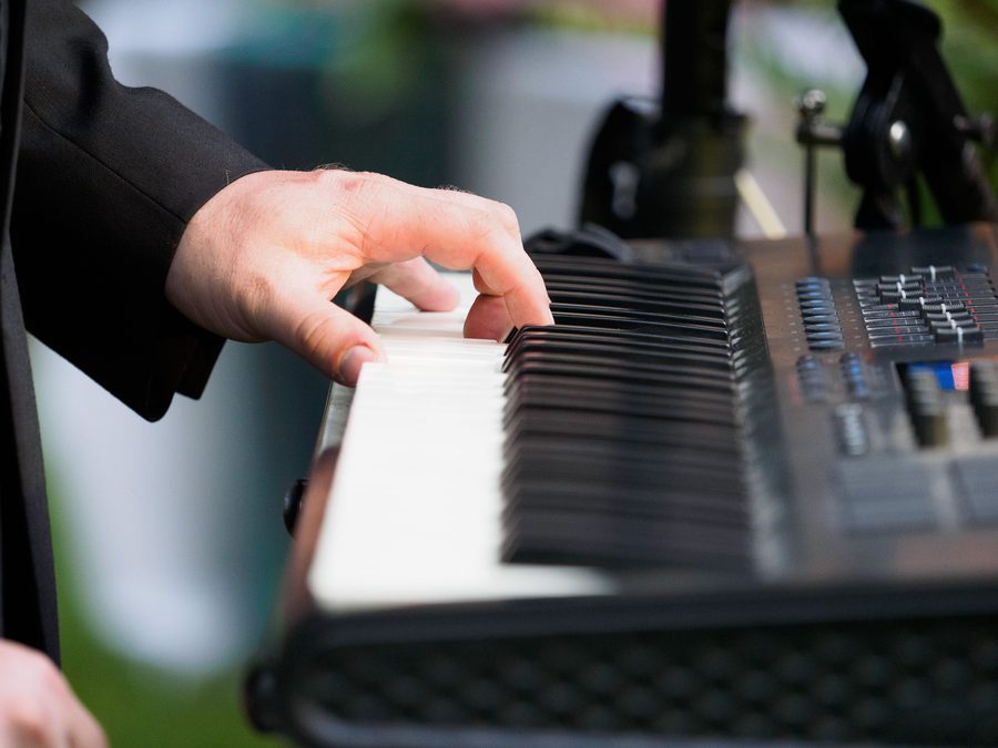 Les mains d'un claviériste sur un synthétiseur, lors d'un concert en plein air.
