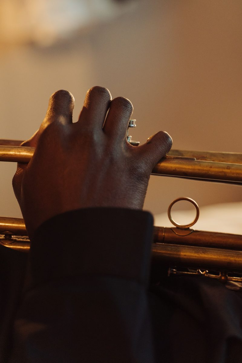 La main d'un musicien posée sur les pistons d'une trompette, en lumière chaude.