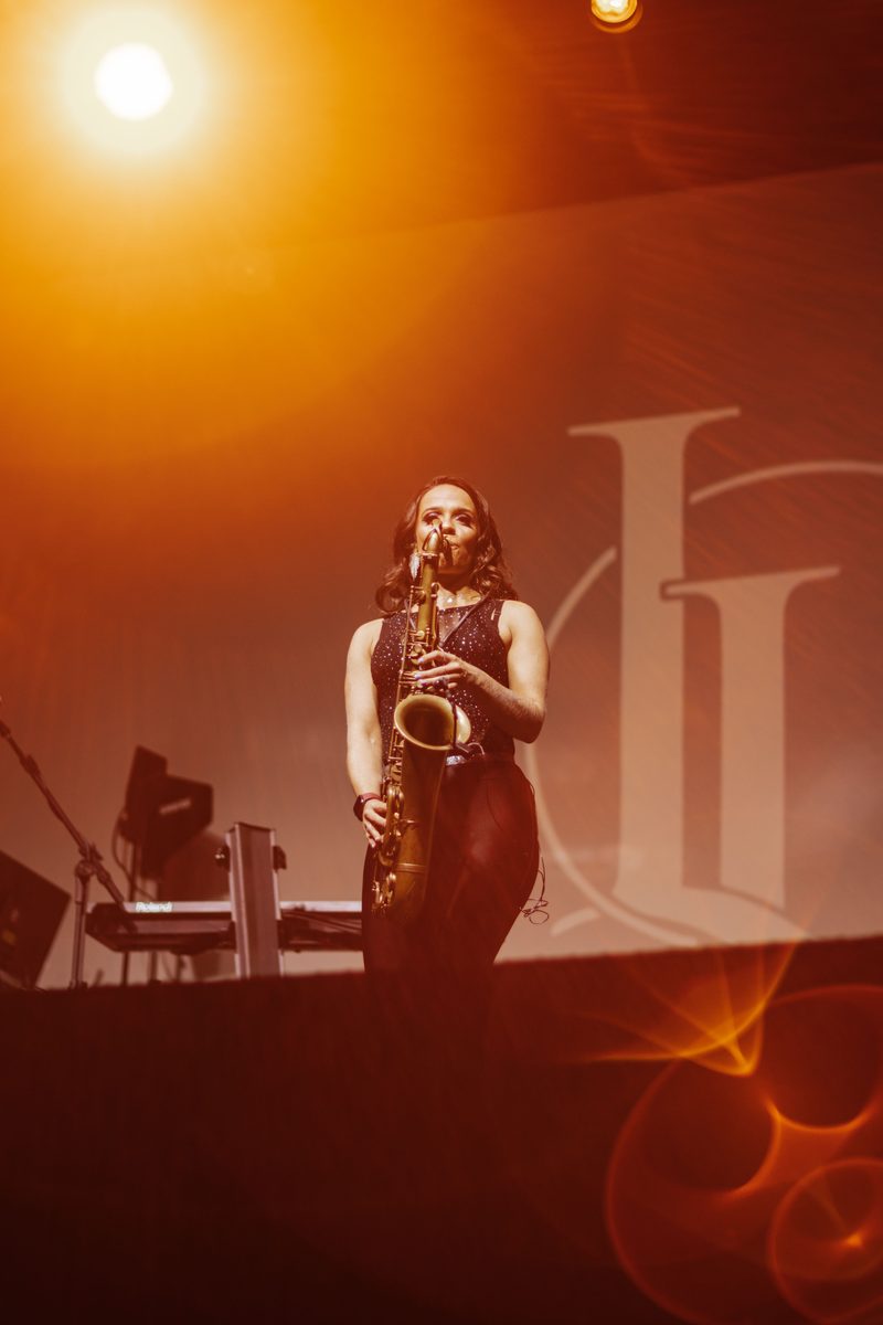 Une saxophoniste joue sur une grande scène baignée de lumière orange.