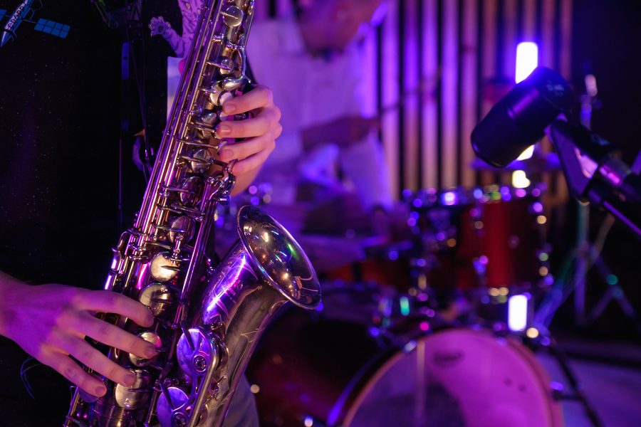 Un saxophoniste joue devant une batterie, sous une lumière violette.